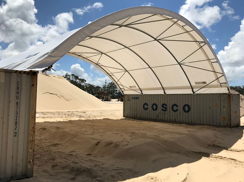Sand Storage Shelter A container-mounted fabric shelter used for storing sand and bulk materials at a construction site.