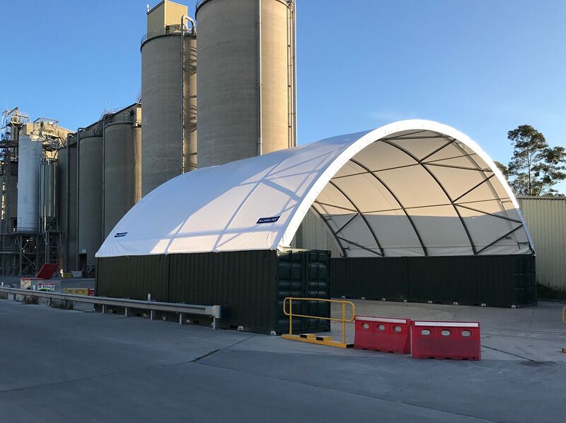 Fabric Shelter Near Silos A container-mounted fabric shelter positioned near industrial silos, providing a covered workspace.